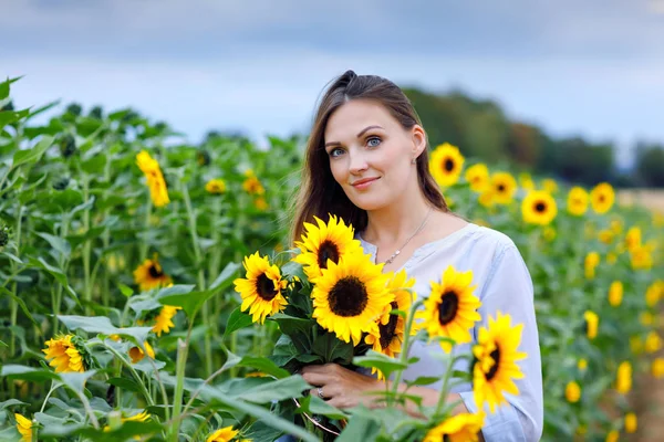 Mooie jonge vrouw op zonnebloemenveld met boeket bloemen. gelukkig meisje op zomer zonsondergang dag. — Stockfoto