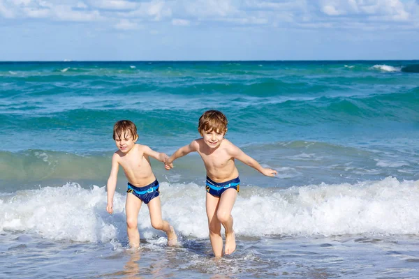 Due ragazzini felici che corrono sulla spiaggia dell'oceano. Bambini simpatici divertenti, fratelli, gemelli e migliori amici che fanno vacanze e si godono l'estate nella tempestosa giornata estiva soleggiata. Miami, Florida — Foto Stock