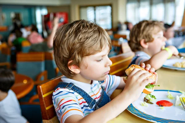 Cute healthy preschool kid boy eats hamburger sitting in school or nursery cafe. Happy child eating healthy organic and vegan food in restaurant. Childhood, health concept. — Stock Photo, Image