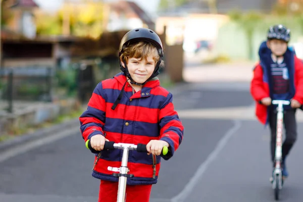 Två små pojkar som åker skoter på väg till eller från skolan. Skolpojkar på 7 år kör genom regnpöl. Roliga syskon och bästa vänner som leker tillsammans. Barn efter skolan — Stockfoto