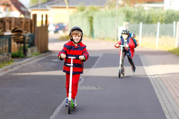 Deux petits garçons sur des scooters poussent sur le chemin de ou vers l'école. Écoliers de 7 ans conduisant dans une flaque d'eau de pluie. Drôle de frères et sœurs et meilleurs amis jouant ensemble. Enfants après l'école — Photo