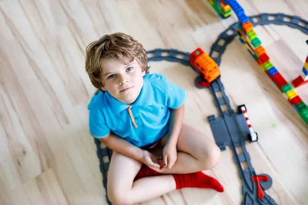Öltöztetős Eunji kis szőke fiú játszani a színes műanyag blokkokat és megteremti a vasútállomástól. Gyermek birtoklás móka-val épület vasúti toys otthon — Stock Fotó