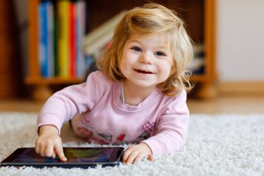 Sevimli küçük yürümeye başlayan çocuk kız evde tablet pc ile oynuyor. Yüzeye parmaklarıyla dokunarak, çizgi film arıyorsunuz ve eğitsel oyunlar ile eğleniyor bilgisayarda sağlıklı bir bebek. Erken geliştirme kavramı