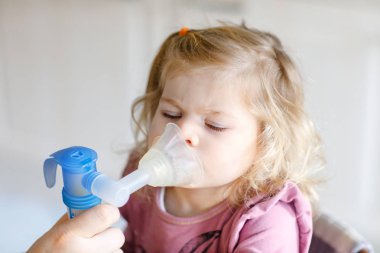 Küçük kız evde nebulizörle nefes alıp veriyor. Baba ya da anne yardım ediyor ve cihazı tutuyor. Çocuk grip, öksürük ve bronşit olmuş. Astım spreyi soluması buhar tutması konsepti