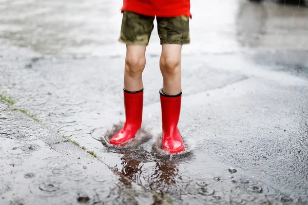 Dítě nosit červený déšť boty, skákání do louže. — Stock fotografie