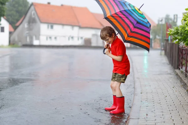Niño usando botas de lluvia rojas y caminando con paraguas — Foto de Stock