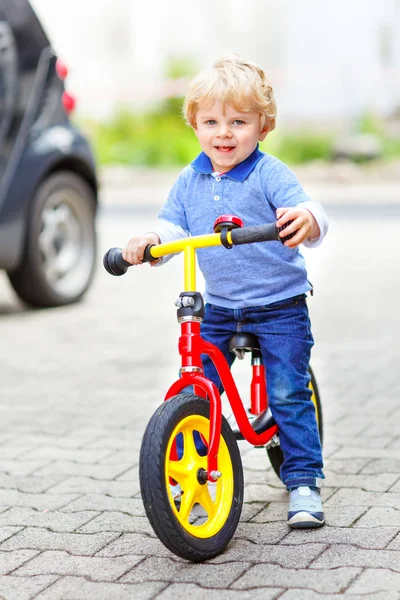 Menino loiro ativo em roupas coloridas que conduzem equilíbrio e aprendizes de bicicleta ou bicicleta no jardim doméstico. Criança sonhando e se divertindo no dia quente de verão. jogo de movimento ao ar livre para crianças — Fotografia de Stock