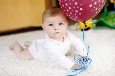 Kırmızı hava balonuyla oynayan şirin bir bebek. Yeni doğmuş çocuk, küçük kız eğleniyor, kavrıyor ve sürünüyor. Aile, yeni hayat, çocukluk, başlangıç konsepti. Bebek yakalama.