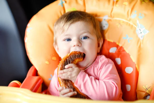 Cute little baby girl eating bread. Child eating for the first time piece of pretzel. First food after breastfeeding. Healthy baby having fun. — Stock Photo, Image