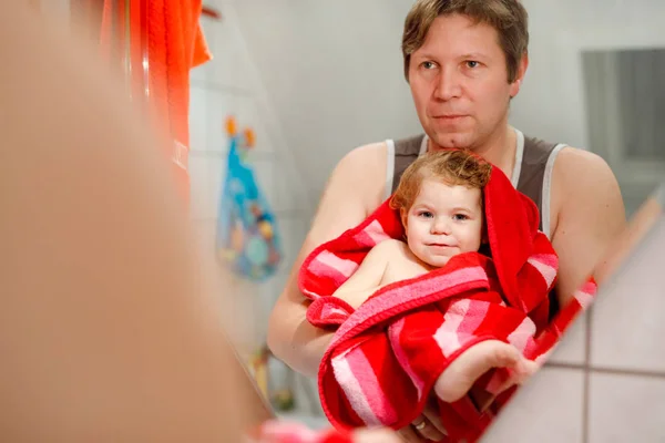 Vader met een schattig klein peutermeisje in een handdoek gewikkeld na het bad. Gelukkig gezond baby kind met natte haren kijken in de spiegel in de badkamer en lachen. Familierelatie van dochter en vader — Stockfoto