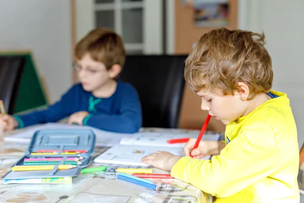 Dois miúdos em casa a fazer trabalhos de casa. Pequenas crianças concentradas escrevendo com lápis coloridos, dentro de casa. Escola primária e educação. Irmãos e melhores amigos aprendendo . — Fotografia de Stock
