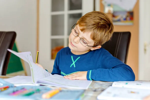 Portrait d'un mignon écolier portant des lunettes à la maison faisant ses devoirs. Petite écriture d'enfant concentrée avec des crayons colorés, à l'intérieur. École primaire et éducation — Photo