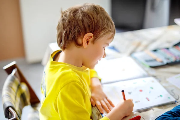Portrétu z cute kid školáka doma dělat domácí úkoly. Psaní s barevné tužky, uvnitř málo koncentrované dítě. Základní škola a vzdělání. Psi učení psaní písmen a číslic. — Stock fotografie