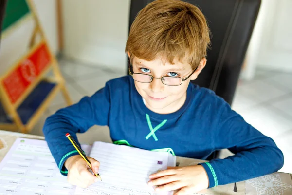 Portrait d'un mignon écolier portant des lunettes à la maison faisant ses devoirs. Petite écriture d'enfant concentrée avec des crayons colorés, à l'intérieur. École primaire et éducation — Photo