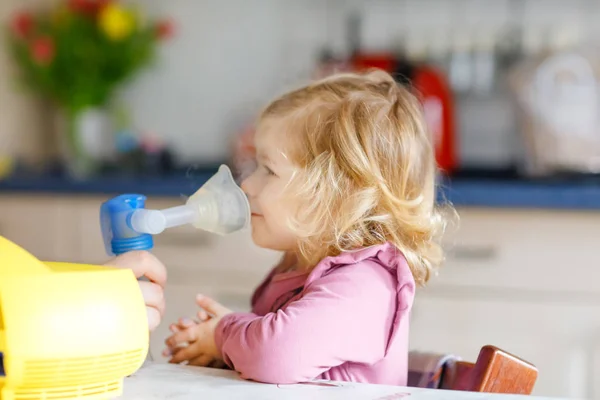 Küçük kız evde nebulizörle nefes alıp veriyor. Baba ya da anne yardım ediyor ve cihazı tutuyor. Çocuk grip, öksürük ve bronşit olmuş. Astım spreyi soluması buhar tutması konsepti — Stok fotoğraf