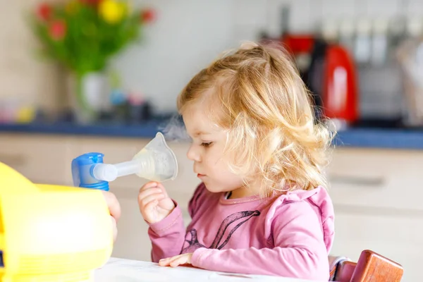En liten flicka som andas in med nebulisator hemma. Far eller mor hjälper och håller i apparaten. Barn som har influensa, hosta och bronkit. koncept för ångsjuka astmainhalatorer — Stockfoto
