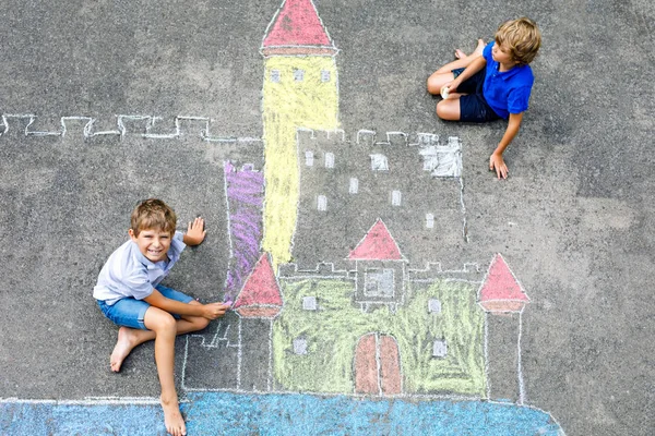 Dua anak laki-laki kecil menggambar benteng ksatria dengan kapur berwarna-warni di aspal. Saudara-saudara yang bahagia dan teman-teman bersenang-senang dengan menciptakan gambar kapur dan lukisan. Waktu luang kreatif untuk anak-anak di musim panas . — Stok Foto