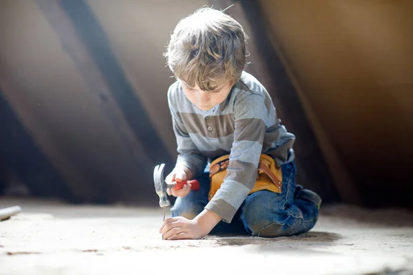 Mały chłopiec pomaga z zabawkami na placu budowy. Zabawne dziecko od 6 lat bawiące się na budowie nowego domu rodzinnego. Dzieciak z gwoździami i młotkiem pomaga ojcu odnowić stary dom. — Zdjęcie stockowe