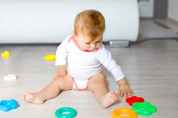 Adorável menina brincando com brinquedos educativos no berçário. Criança saudável feliz se divertindo com brinquedos diferentes coloridos em casa. Criança tentando construir pirâmide de plástico e usando blocos com letras — Fotografia de Stock