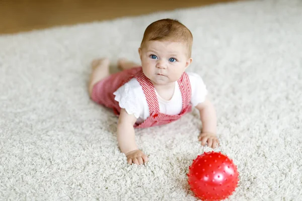 Söt baby leker med röda tuggummi boll. Naturliga flicka tittar på kameran och kryper. Familj, nytt liv, barndom, början koncept. Baby lärande grab. — Stockfoto