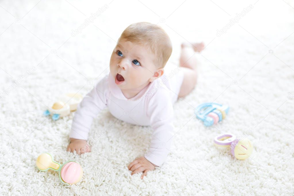 Cute baby playing with colorful pastel vintage rattle toy. New born child, little girl looking at the camera and crawling. Family, new life, childhood, beginning concept. Baby learning grab.