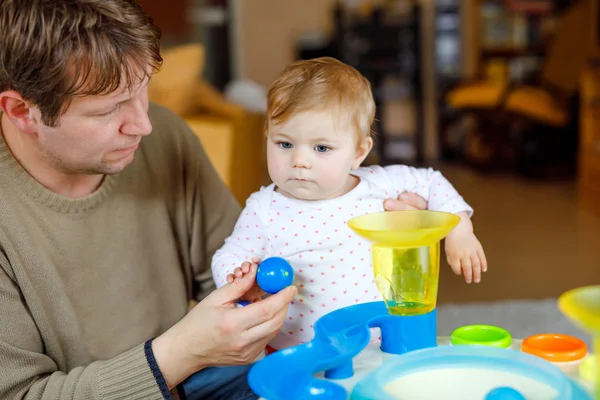 Gelukkig trotse jonge vader plezier met baby dochter, familieportret samen. Papa spelen met babymeisje met educatieve sorter speelgoed met verschillende kleurrijke ballen. Man met klein kind thuis. — Stockfoto