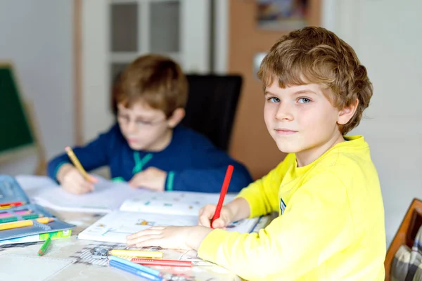Två små barn pojkar hemma att göra läxor. Lite koncentrerad barn skriver med färgglada pennor, inomhus. Folkskola samt utbildning. Syskon och bästa vänner lärande. — Stockfoto