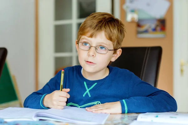 Portrait d'un mignon écolier portant des lunettes à la maison faisant ses devoirs. Petite écriture d'enfant concentrée avec des crayons colorés, à l'intérieur. École primaire et éducation — Photo