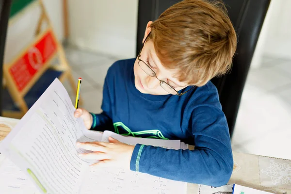 Ritratto di ragazzo carino della scuola con gli occhiali a casa a fare i compiti. Piccolo bambino concentrato che scrive con matite colorate, al chiuso. Scuola elementare e istruzione — Foto Stock