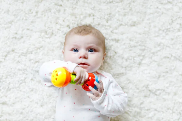 Leuke schattige pasgeboren baby spelen met kleurrijke rammelaar speelgoed op witte achtergrond. Nieuw geboren kindje, kleine meisje te kijken naar de camera. Familie, nieuw leven, kindertijd, begin concept. Baby leren pak. — Stockfoto