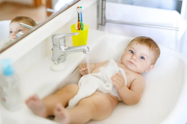 Bebê adorável bonito tomando banho na pia de lavagem e pegar torneira de água. Menina saudável com grandes olhos azuis se divertindo. Limpar bela criança brincando — Fotografia de Stock