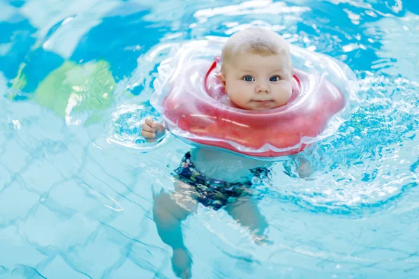 Schattig klein baby kind leren om te zwemmen met zwemmen ring in een overdekt zwembad. pasgeboren meisje of jongen plezier in water. Actieve gezonde ontspannings- en sportapparatuur voor baby's en kinderen. — Stockfoto
