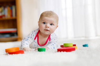 Yeni doğmuş şirin bebek beyaz arka planda renkli tahta çıngıraklı oyuncak topuyla oynuyor. Yeni doğmuş bir çocuk, kameraya bakan küçük bir kız. Aile, yeni hayat, çocukluk, başlangıç konsepti.