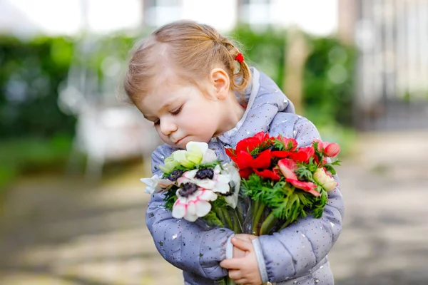 Pequeña niña encantadora con flores de ranúnculo rojo y blanco en el jardín de primavera. Feliz lindo bebé sosteniendo fresco ramo de colores como regalo para el día de las madres para mamá. — Foto de Stock