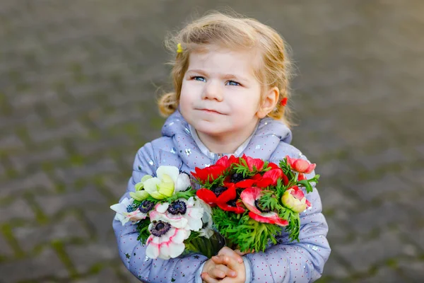 Piccolo bambino bella ragazza con fiori ranuncoli rossi e bianchi nel giardino primaverile. Felice bambino carino tenendo fresco bouquet colorato come regalo per la giornata delle madri per la mamma. — Foto Stock
