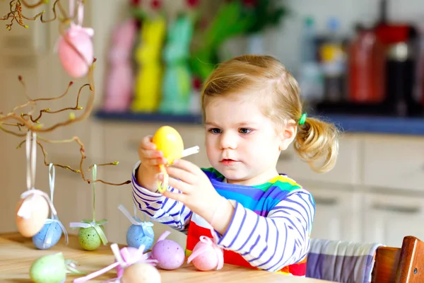 Cute little toddler girl decorating tree bough with colored pastel plastic eggs. Happy baby child having fun with Easter decorations. Adorable healthy smiling kid in enjoying family holiday — Stock Photo, Image