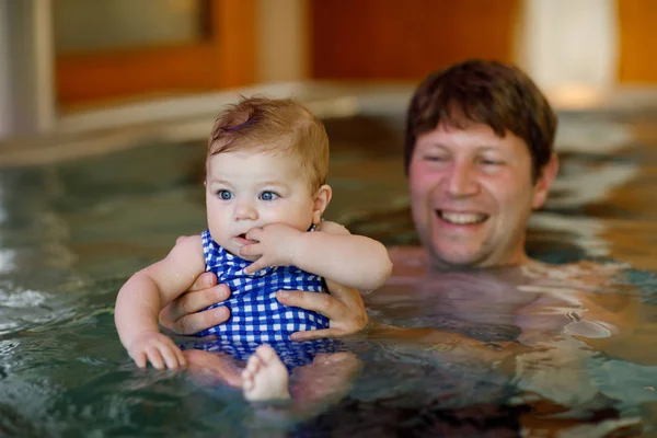 Happy middle-aged father swimming with cute adorable baby daughter in whirl pool. Smiling dad and little child, girl of 6 months having fun together. Active family spending leisure in spa hotel