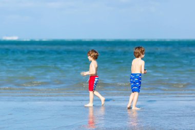 İki küçük çocuklar dostluk kavramı eğleniyor tropik sahilde oynarken, mutlu arkadaşlarım çocuğu. Kardeş kardeş, İkizler aile arka plan üzerinde avuç içi ile bak. Okyanus üzerinde aile tatil.