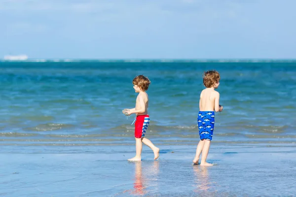 Två barn lite pojkar ha kul på tropical beach, happy bästa vänner spelar, vänskap koncept. Syskon bröder, tvillingar i familjen ser med handflatorna på bakgrunden. Familjens semester på ocean. — Stockfoto