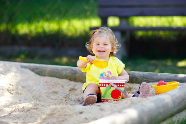 Menina bonito brincando na areia no parque infantil ao ar livre. Bebê bonito se divertindo no verão quente ensolarado dia ensolarado. Criança saudável feliz com brinquedos de areia e em roupas de moda coloridas. — Fotografia de Stock