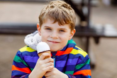 Kıvırcık saçlı küçük sarışın okul çocuk çocuk dondurma konisi yiyor, sıcak güneşli bir günde açık havada waffle ile. Mutlu sağlıklı çocuk dondurma, tatlı tatlı hakkında memnun.