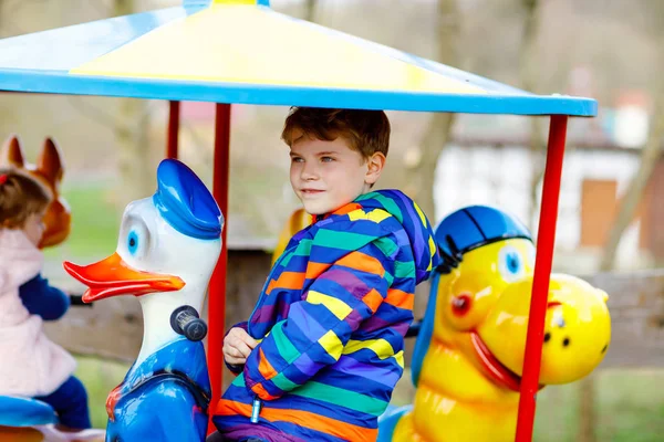 Adorable garçon enfant chevauchant sur animal sur carrousel rond-point dans le parc d'attractions. Heureux écolier en bonne santé s'amuser à l'extérieur le jour ensoleillé. Mauvaise herbe familiale ou vacances — Photo