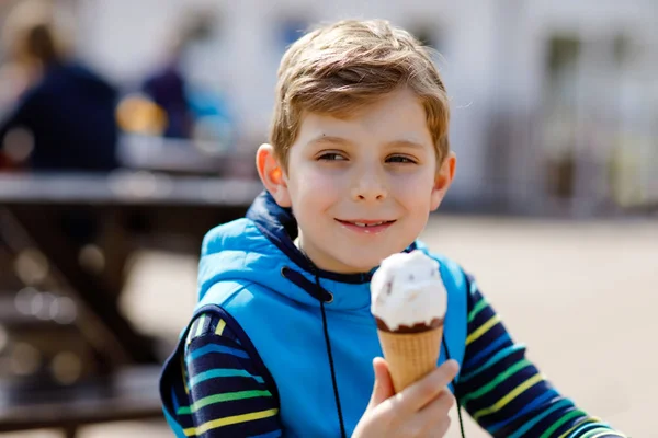 Niño rubio de escuela con pelos rizados comiendo cono de helado, con waffle al aire libre en un día cálido y soleado. Feliz niño sano está contento con el helado, postre dulce . — Foto de Stock