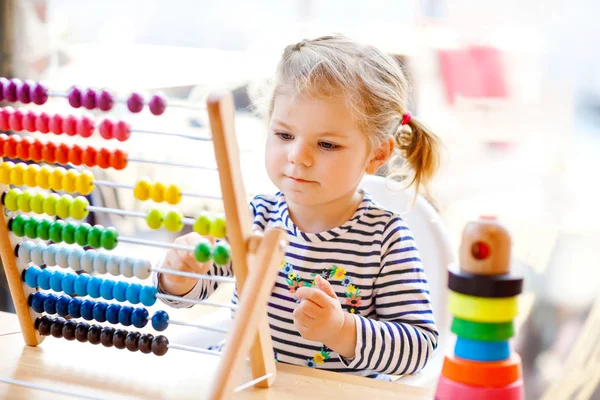 Adorável bonito linda menina criança brincando com pirâmide de brinquedos de madeira educacional arco-íris e contra-ábaco. Bebê feliz saudável aprendendo a contar e cores, dentro de casa no dia ensolarado . — Fotografia de Stock