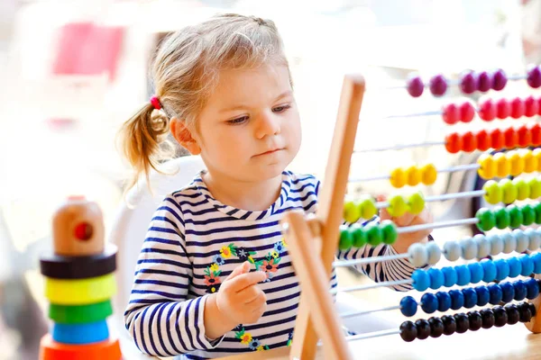 Adorável bonito linda menina criança brincando com pirâmide de brinquedos de madeira educacional arco-íris e contra-ábaco. Bebê feliz saudável aprendendo a contar e cores, dentro de casa no dia ensolarado . — Fotografia de Stock