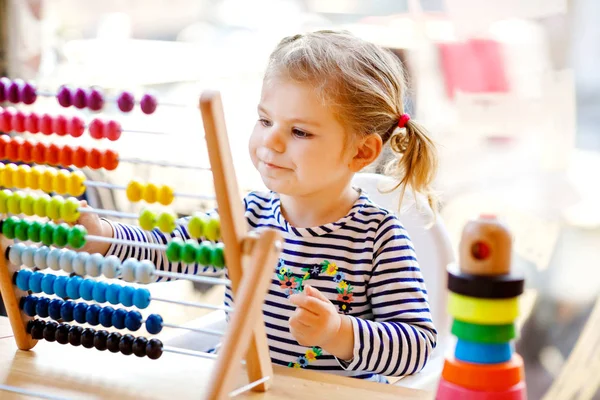 可爱的可爱的可爱的小幼儿女孩玩教育木制彩虹玩具金字塔和反算盘。健康快乐的婴儿学习计数和颜色，在阳光明媚的日子在室内. — 图库照片