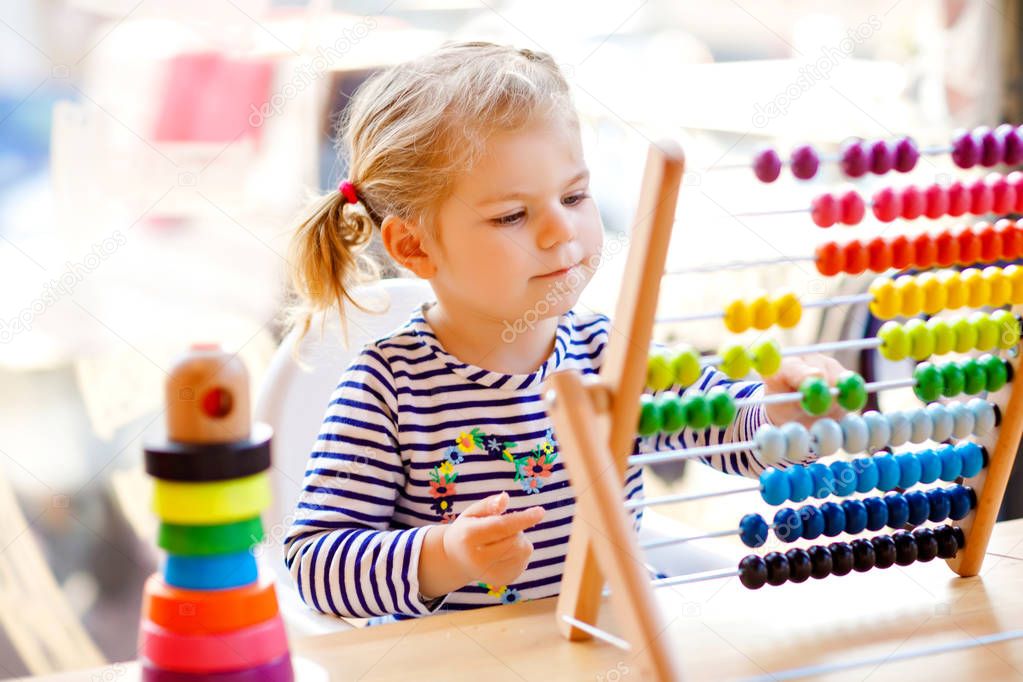 Adorable cute beautiful little toddler girl playing with educational wooden rainbow toy pyramid and counter abacus. Healthy happy baby learning to count and colors, indoors on sunny day.