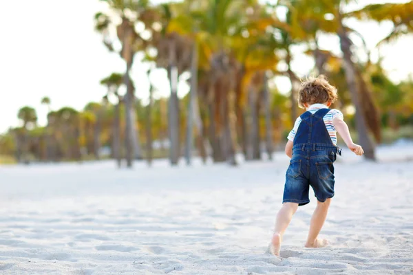 Adorable active little kid boy having fun on Miami beach, Key Biscayne. Happy cute child relaxing, playing with sand and enjoying sunny warm day near palms and ocean — Stock Photo, Image