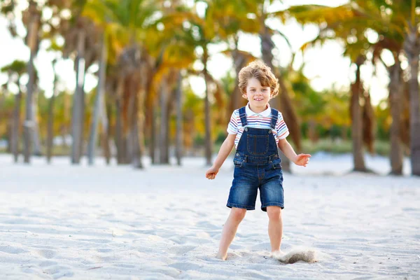 Adorable petit garçon actif qui s'amuse sur la plage de Miami, Key Biscayne. Joyeux enfant mignon relaxant, jouant avec le sable et profitant d'une journée chaude ensoleillée près des paumes et de l'océan — Photo