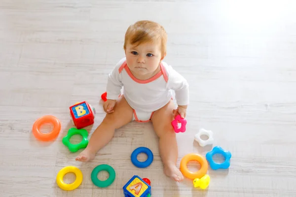 Schattig babymeisje spelen met de educatief speelgoed in de kinderkamer. Gelukkig gezond kind plezier met kleurrijke verschillende speelgoed thuis. Kind proberen kunststof piramide te bouwen en het gebruik van blokken met letters — Stockfoto